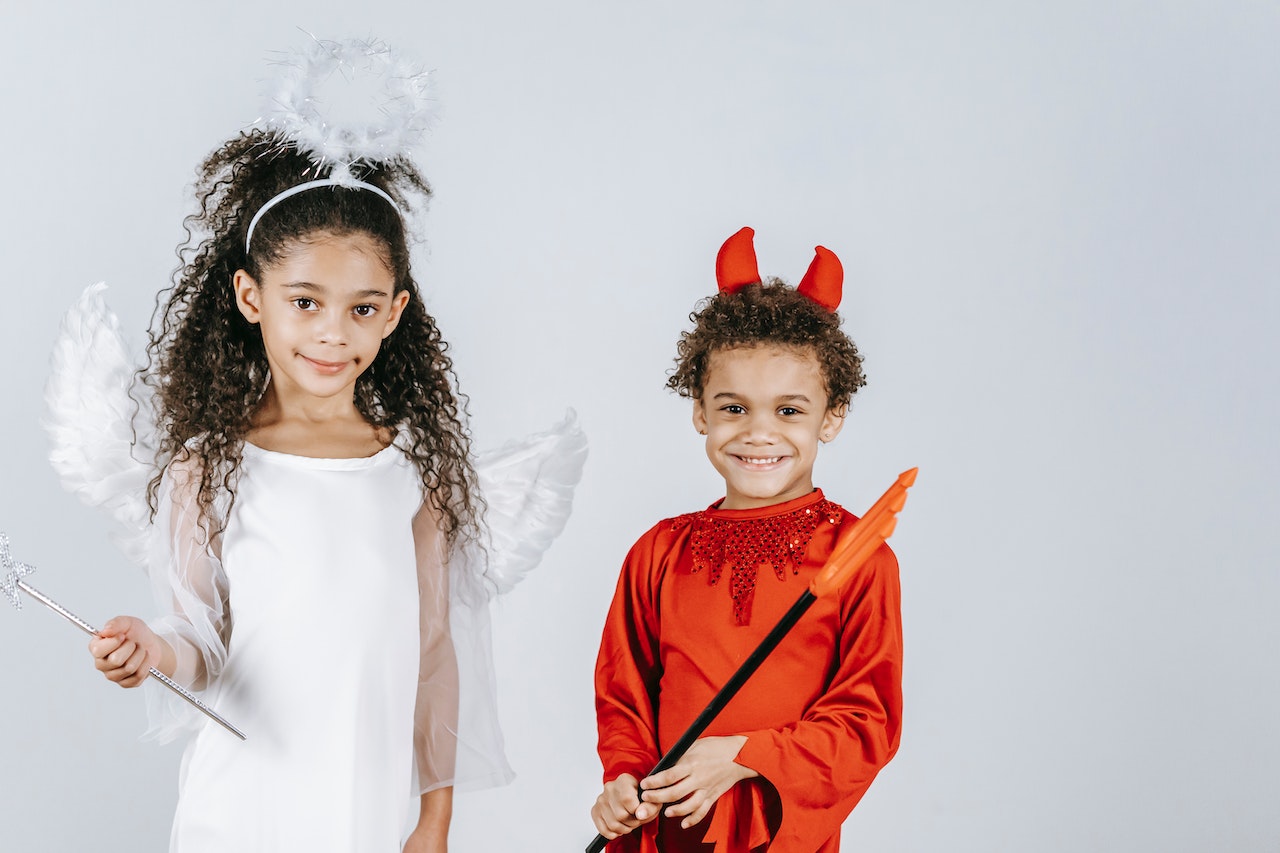 Cute little children in angel and devil costumes smiling at camera in white studio