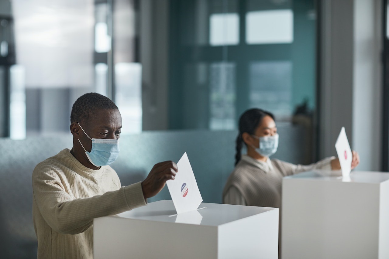 A Black man and an Asian American woman both wearing a face mask cast their votes