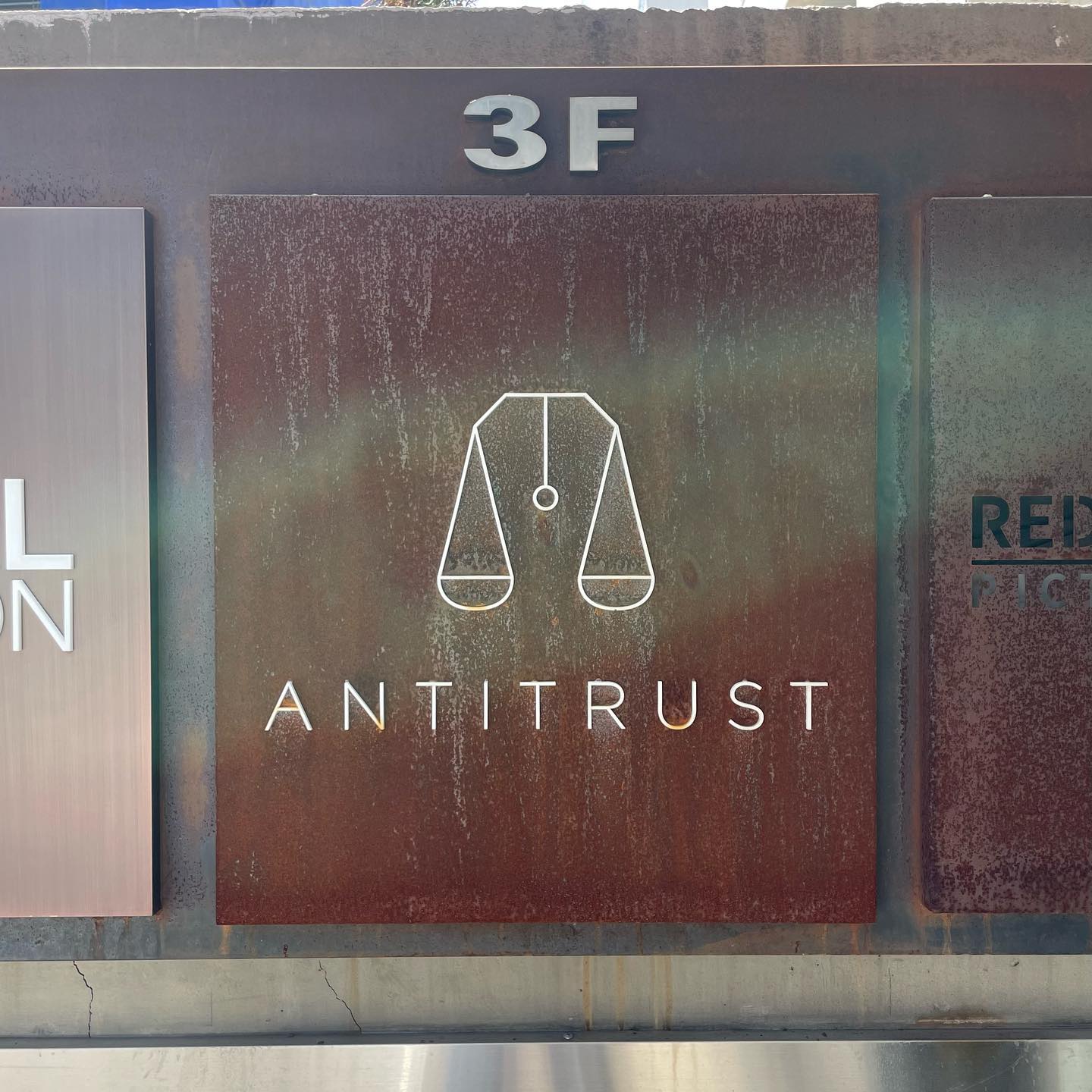 A sign engraved on a square tile, with the word ‘antitrust’ in uppercase letters a balance scale symbol