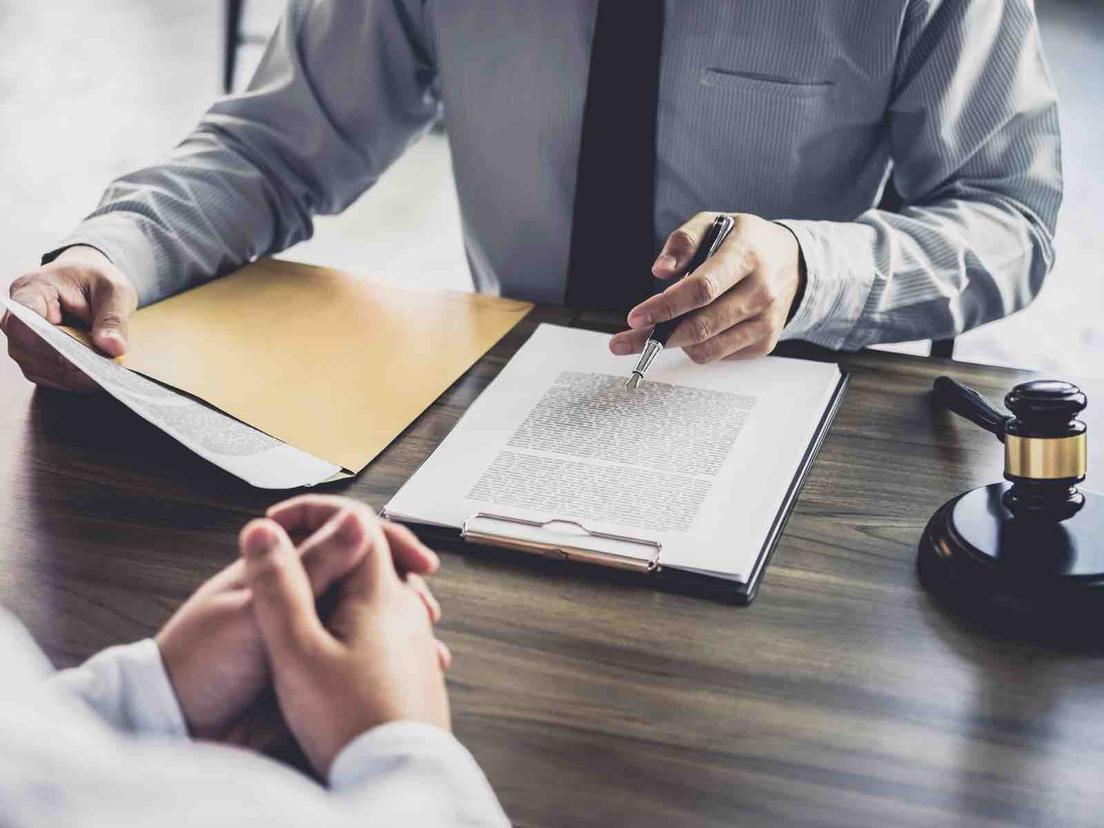 A man in long sleeves polo holding a pen and papers with gavel on the side and a man in front of him